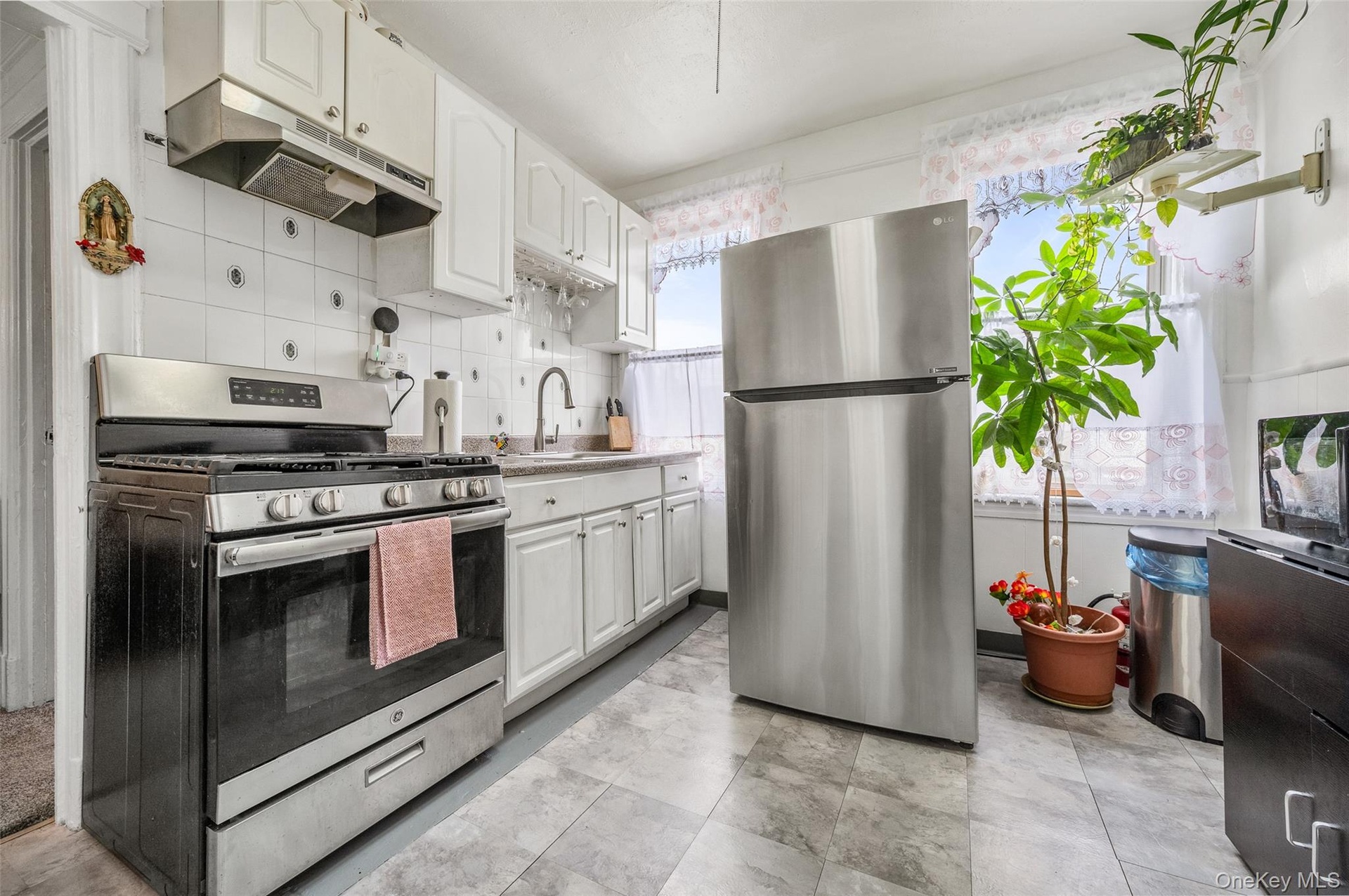 Kitchen with stainless steel appliances, decorative backsplash, under cabinet range hood, white cabinets, and light countertops