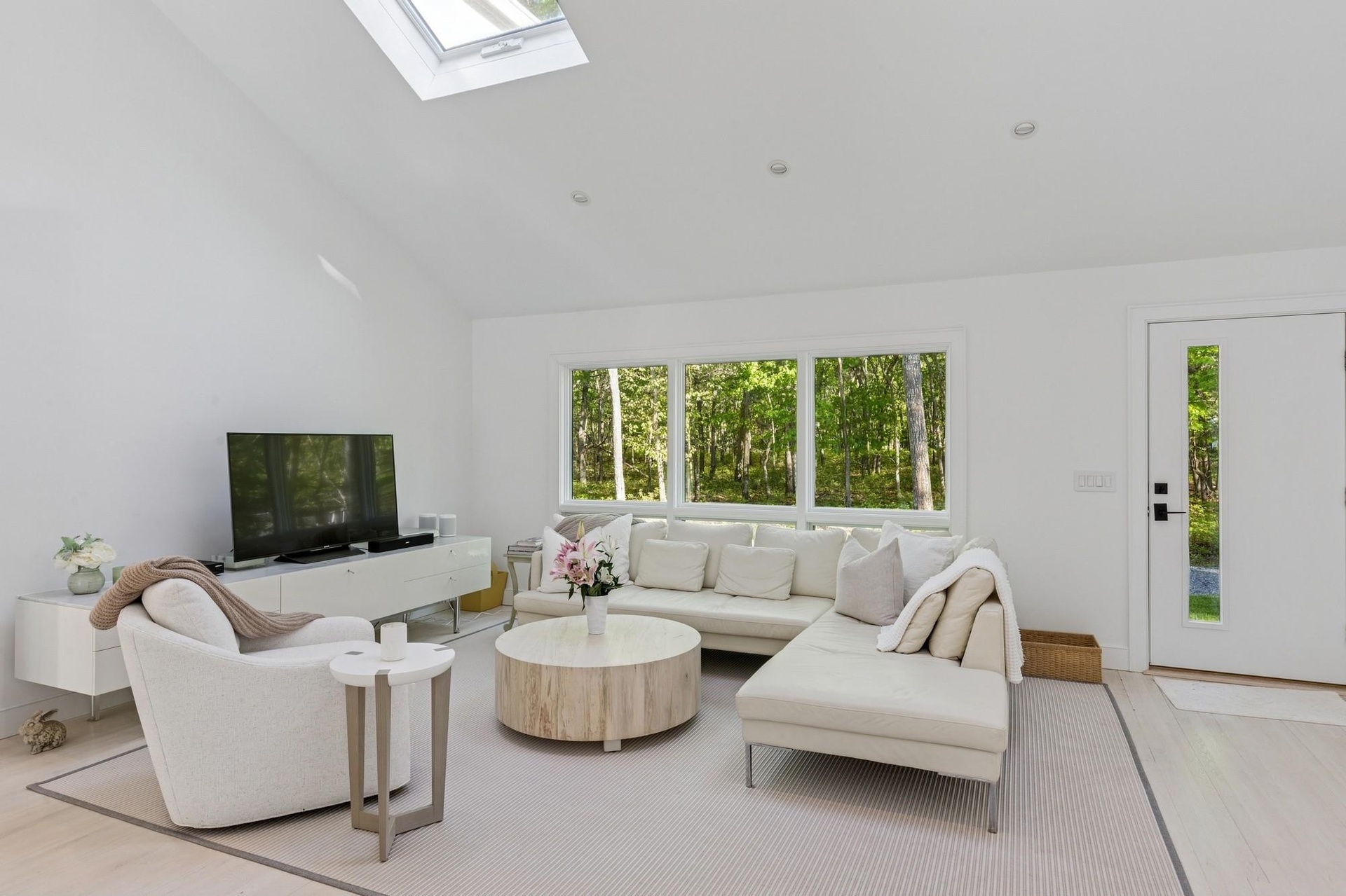 Living room with light wood-type flooring, high vaulted ceiling, and a skylight