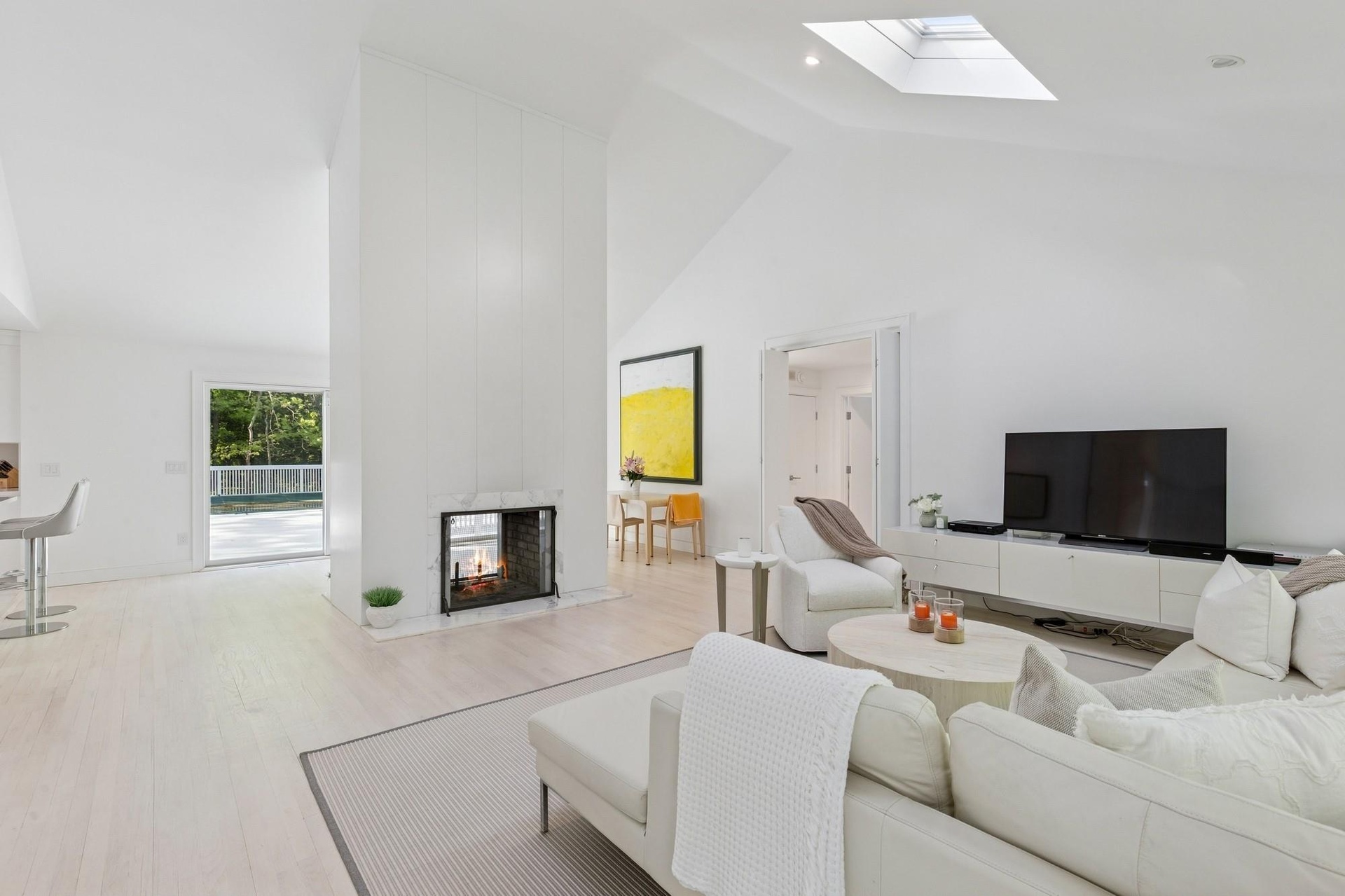 Living room featuring high vaulted ceiling, a skylight, wood finished floors, and a multi sided fireplace