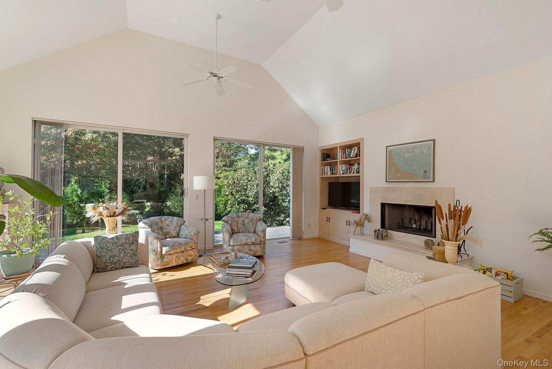 Living area featuring high vaulted ceiling, a tiled fireplace, light wood finished floors, built in features, and ceiling fan