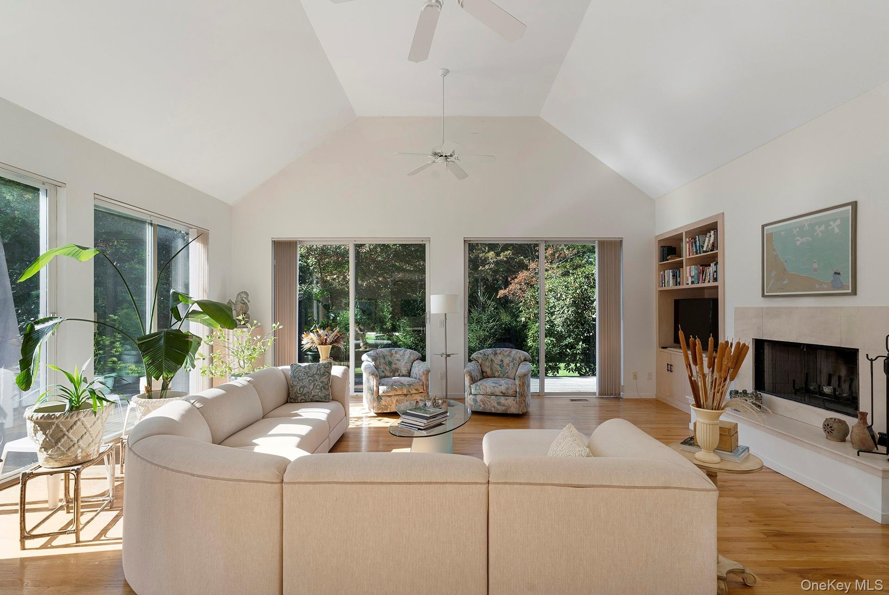 Living area with light wood-type flooring, a high end fireplace, high vaulted ceiling, and built in shelves