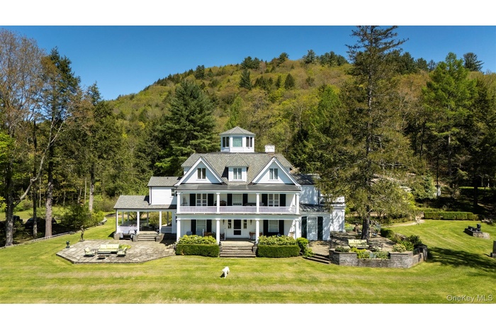 Shingle-style home featuring covered porch, a view of trees, a front yard, and a patio area