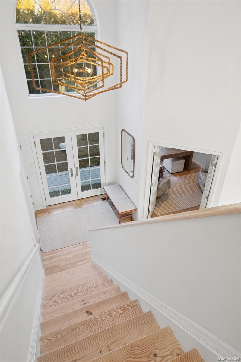 Staircase with a high ceiling, french doors, wood finished floors, and a chandelier