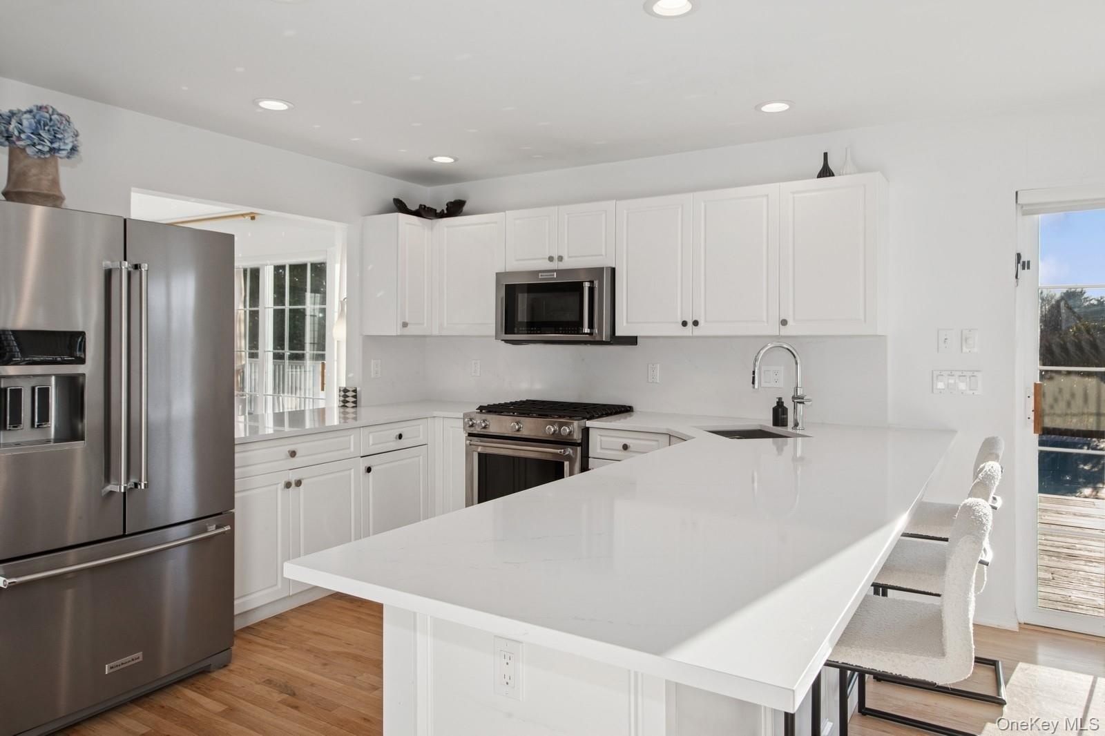 Kitchen with stainless steel appliances, white cabinets, light wood-style flooring, a breakfast bar, and recessed lighting