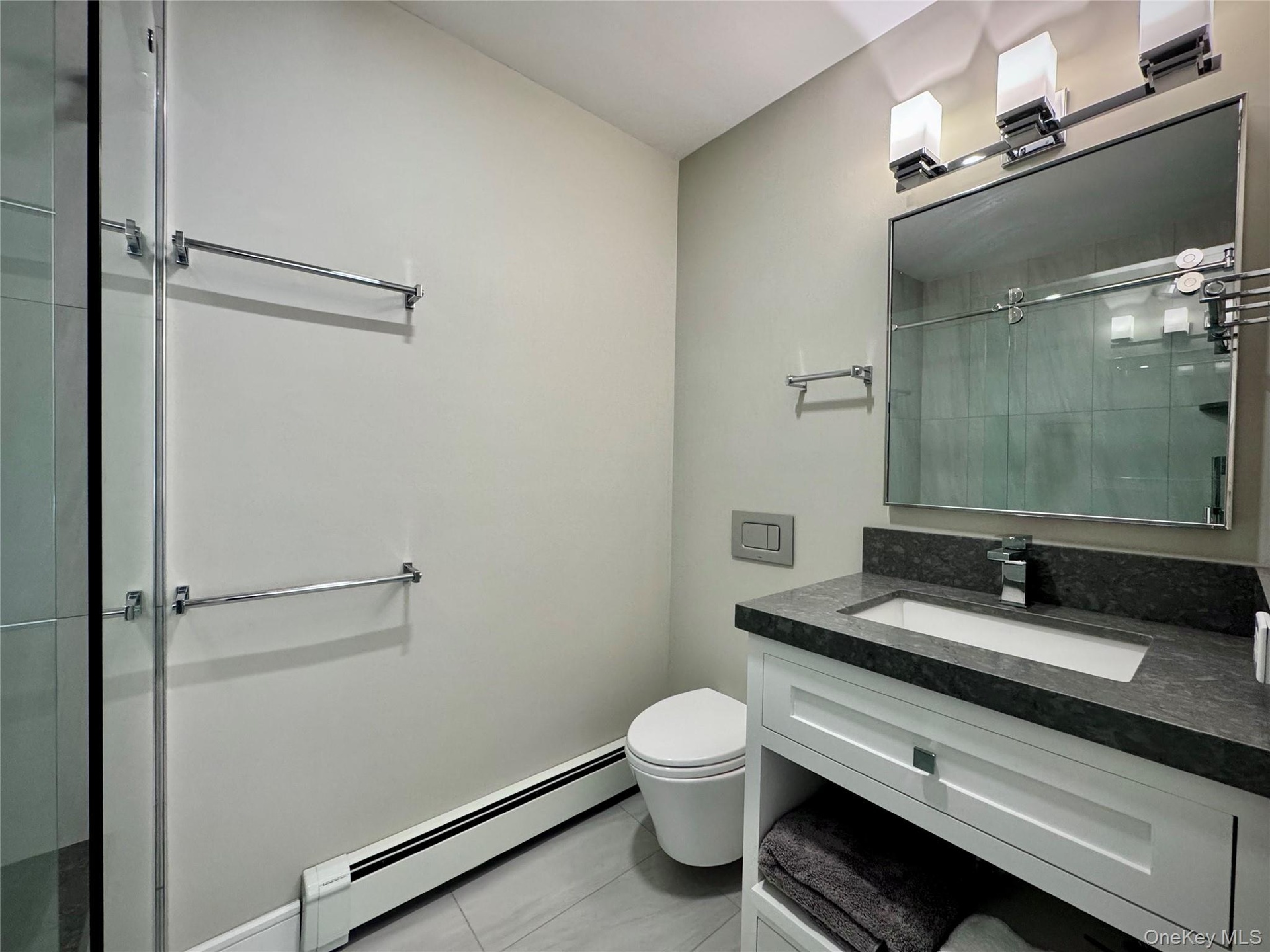 Bathroom with baseboard heating, vanity, light tile patterned floors, and a stall shower