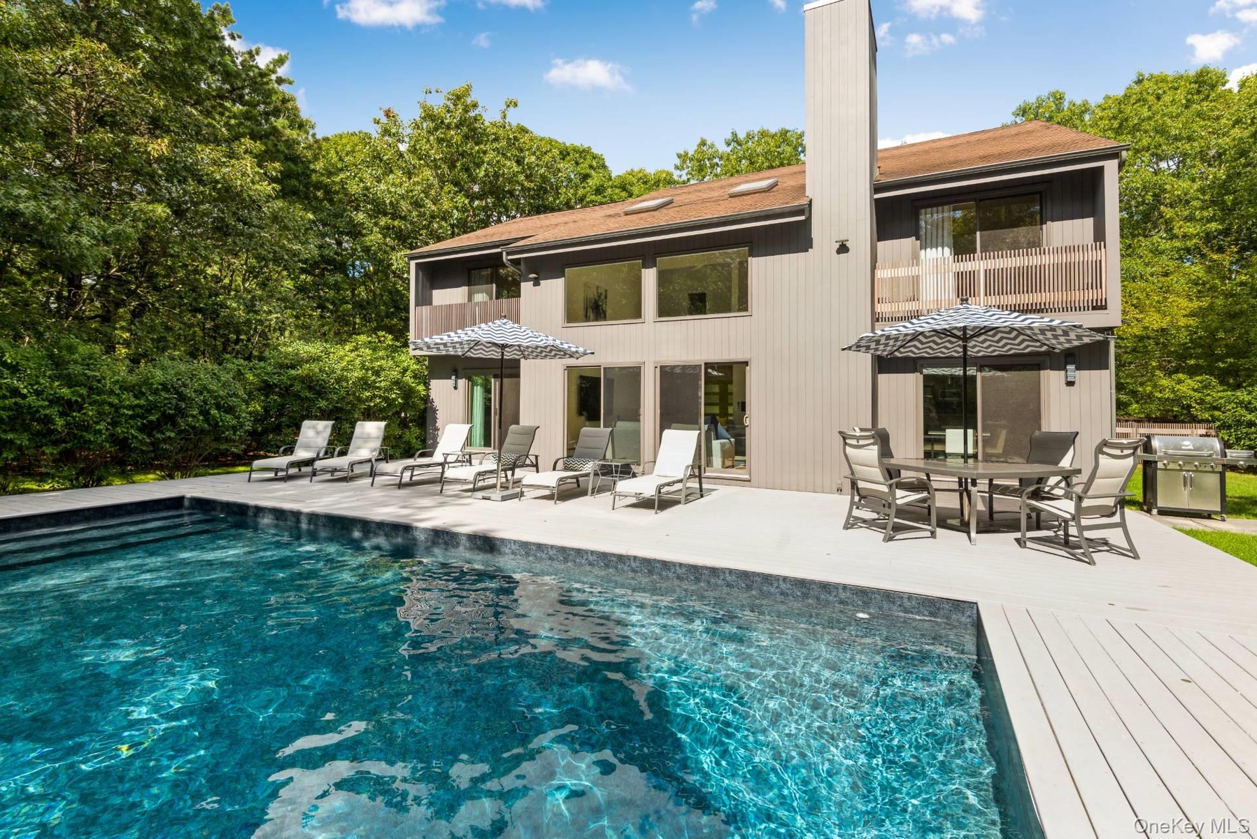 Back of property with an outdoor pool, outdoor dining space, a patio area, and a wooden deck