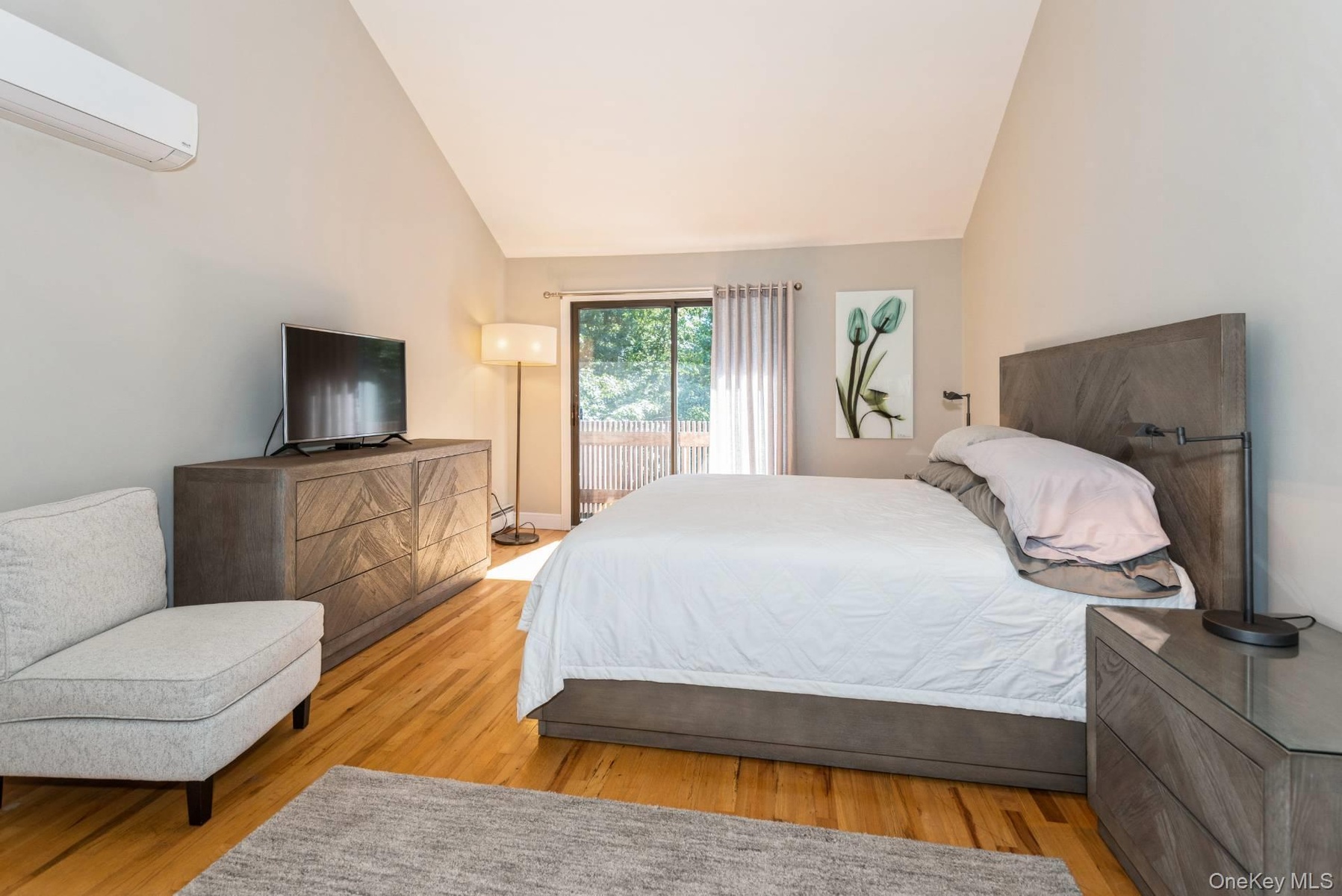 Bedroom featuring a wall mounted air conditioner, access to outside, vaulted ceiling, and wood finished floors