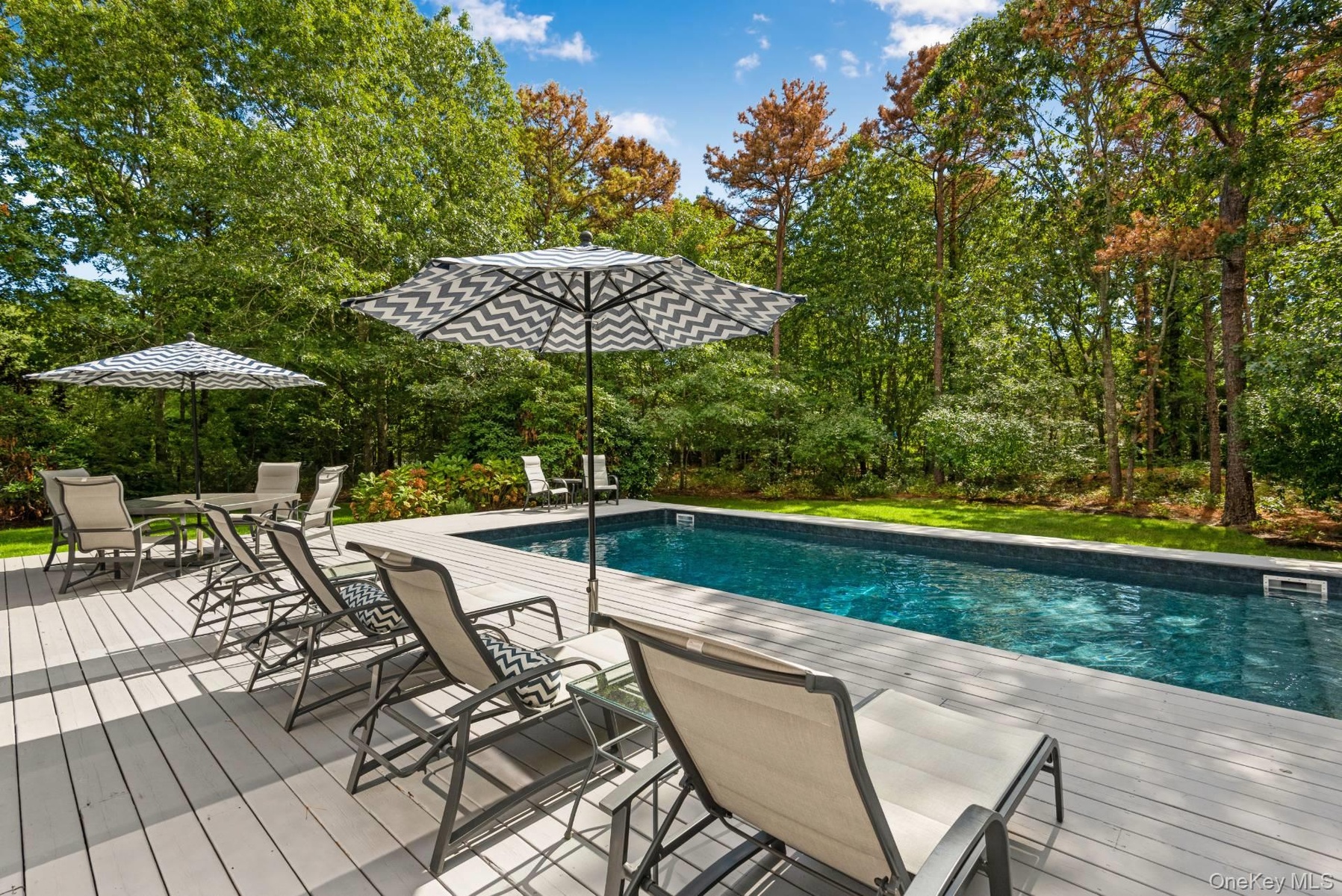 Outdoor pool featuring a deck, outdoor dining area, and view of wooded area