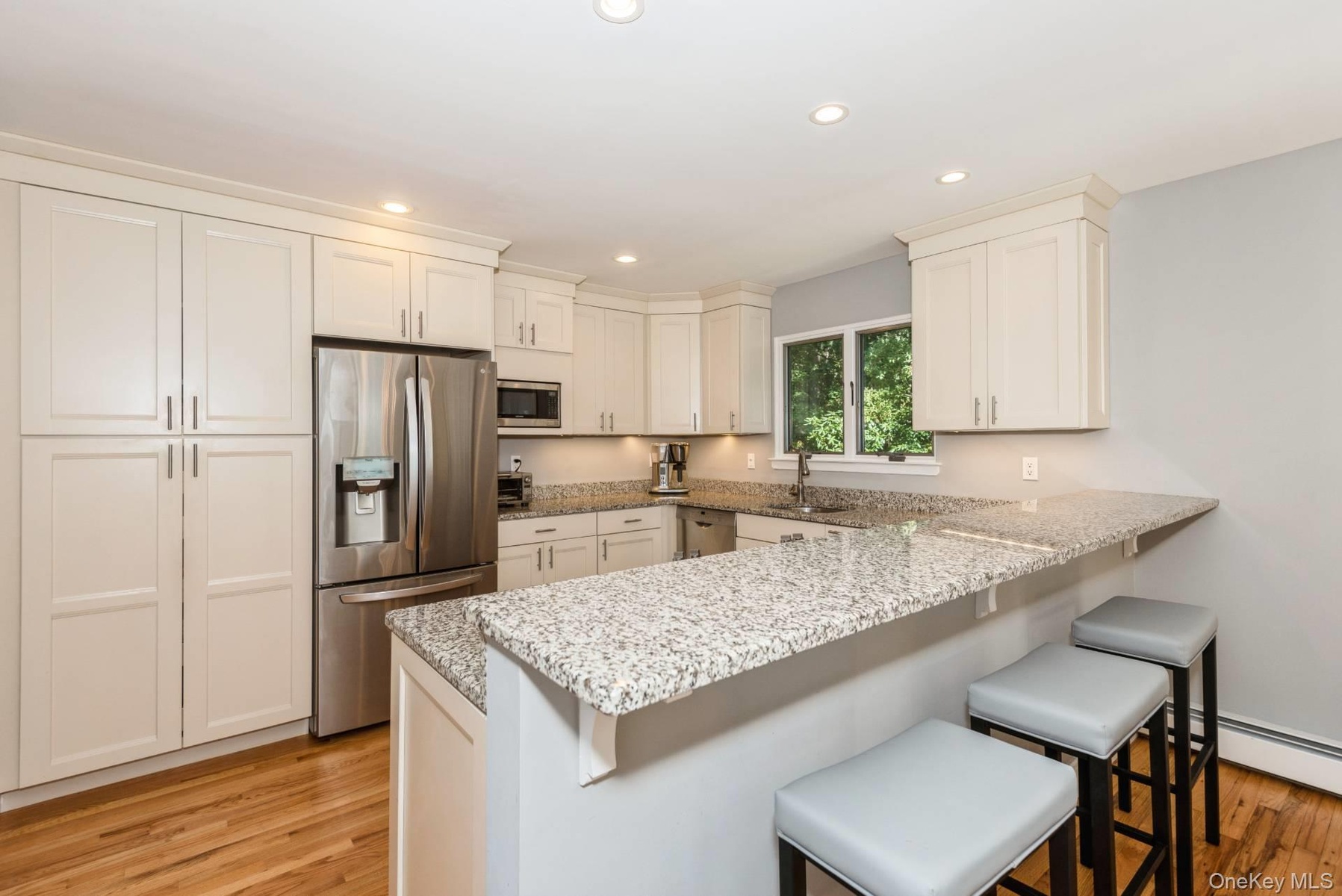 Kitchen with stainless steel appliances, a kitchen bar, a peninsula, white cabinets, and recessed lighting