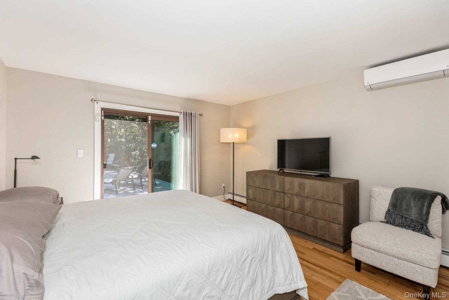 Bedroom featuring light wood-type flooring, access to exterior, a wall mounted air conditioner, and baseboard heating