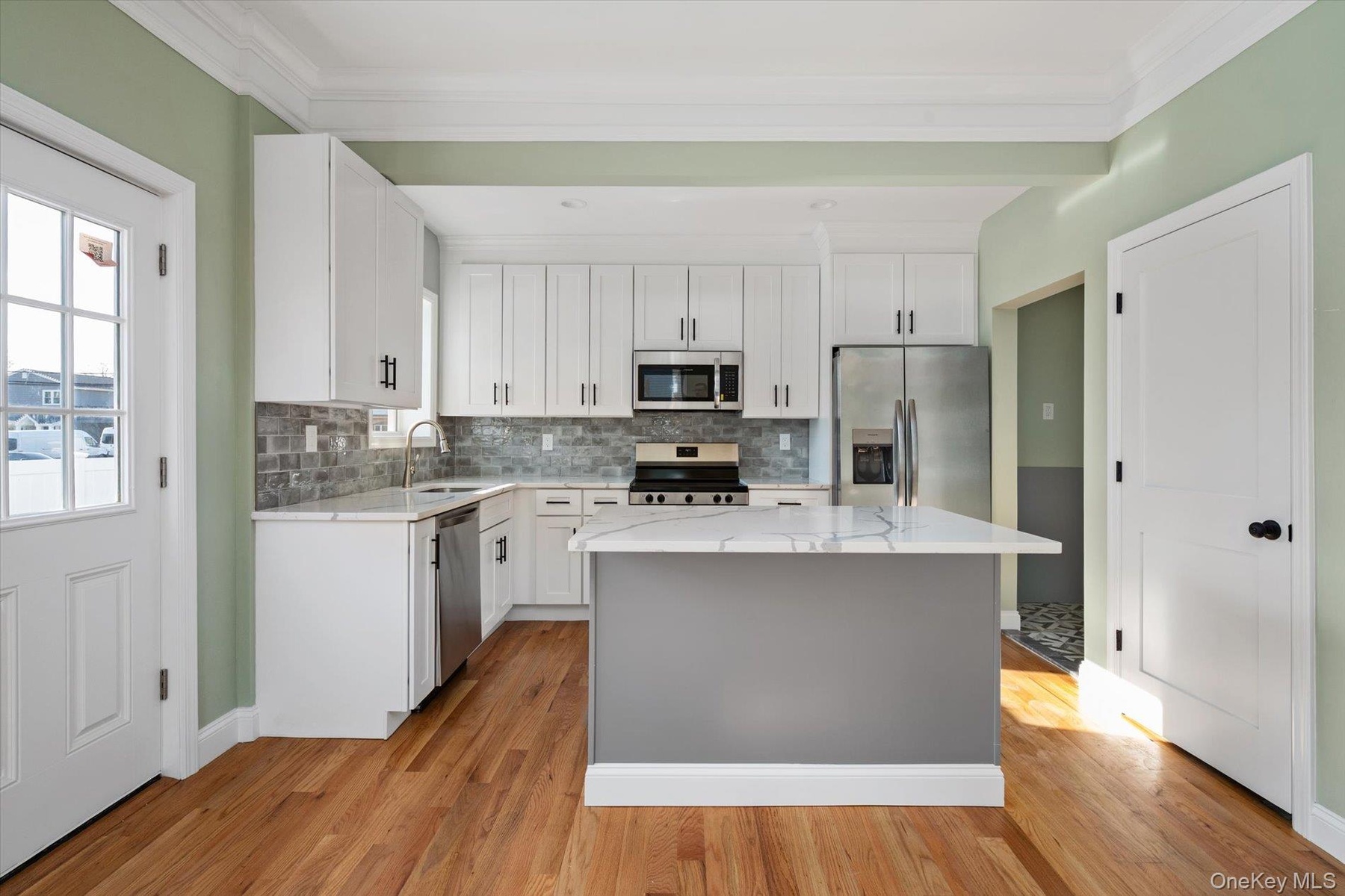 Kitchen featuring light stone countertops, white cabinetry, stainless steel appliances, ornamental molding, and light wood finished floors