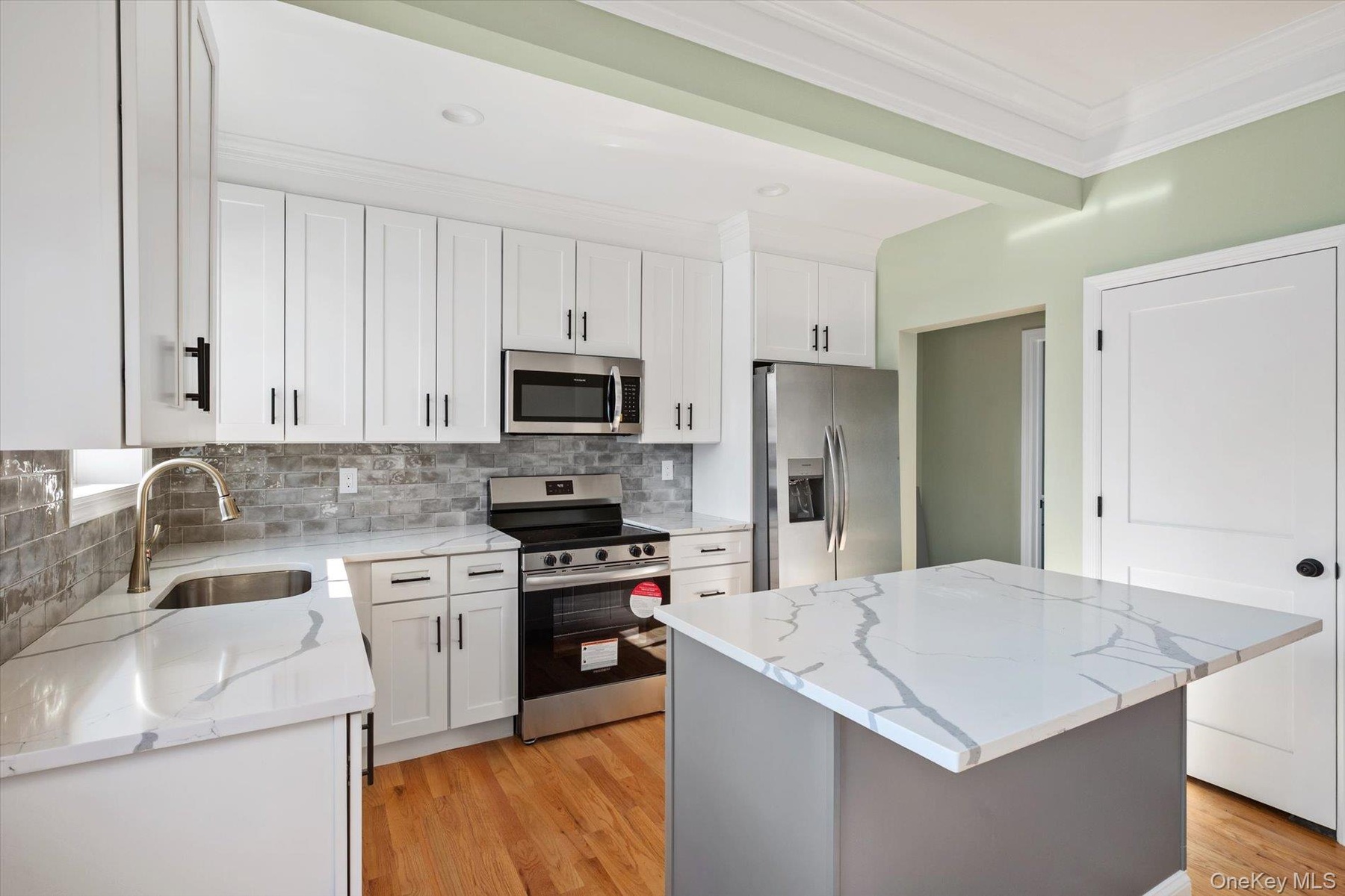 Kitchen featuring stainless steel appliances, white cabinets, a center island, light stone counters, and ornamental molding