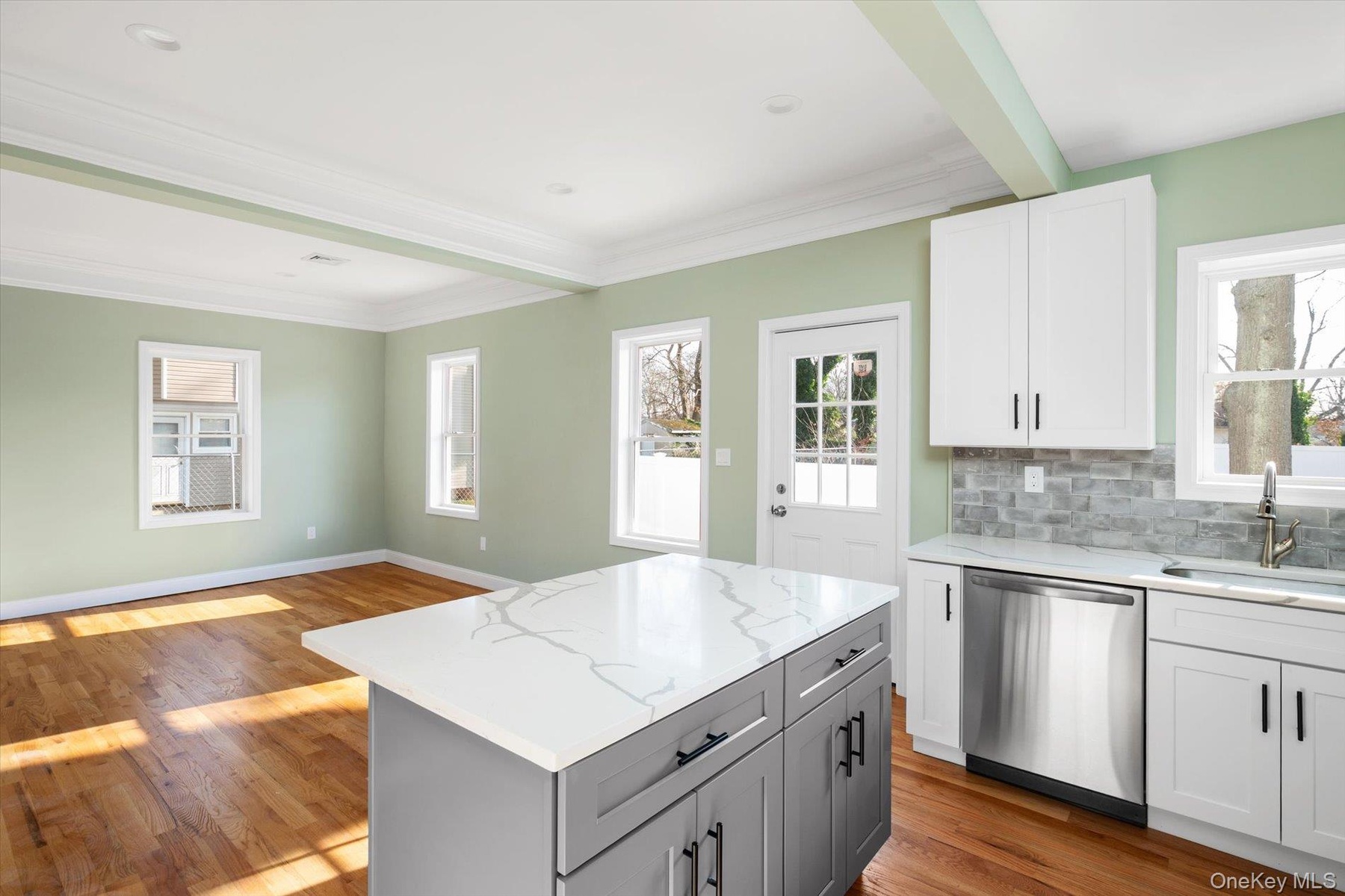 Kitchen featuring white cabinetry, stainless steel dishwasher, light stone counters, gray cabinetry, and crown molding