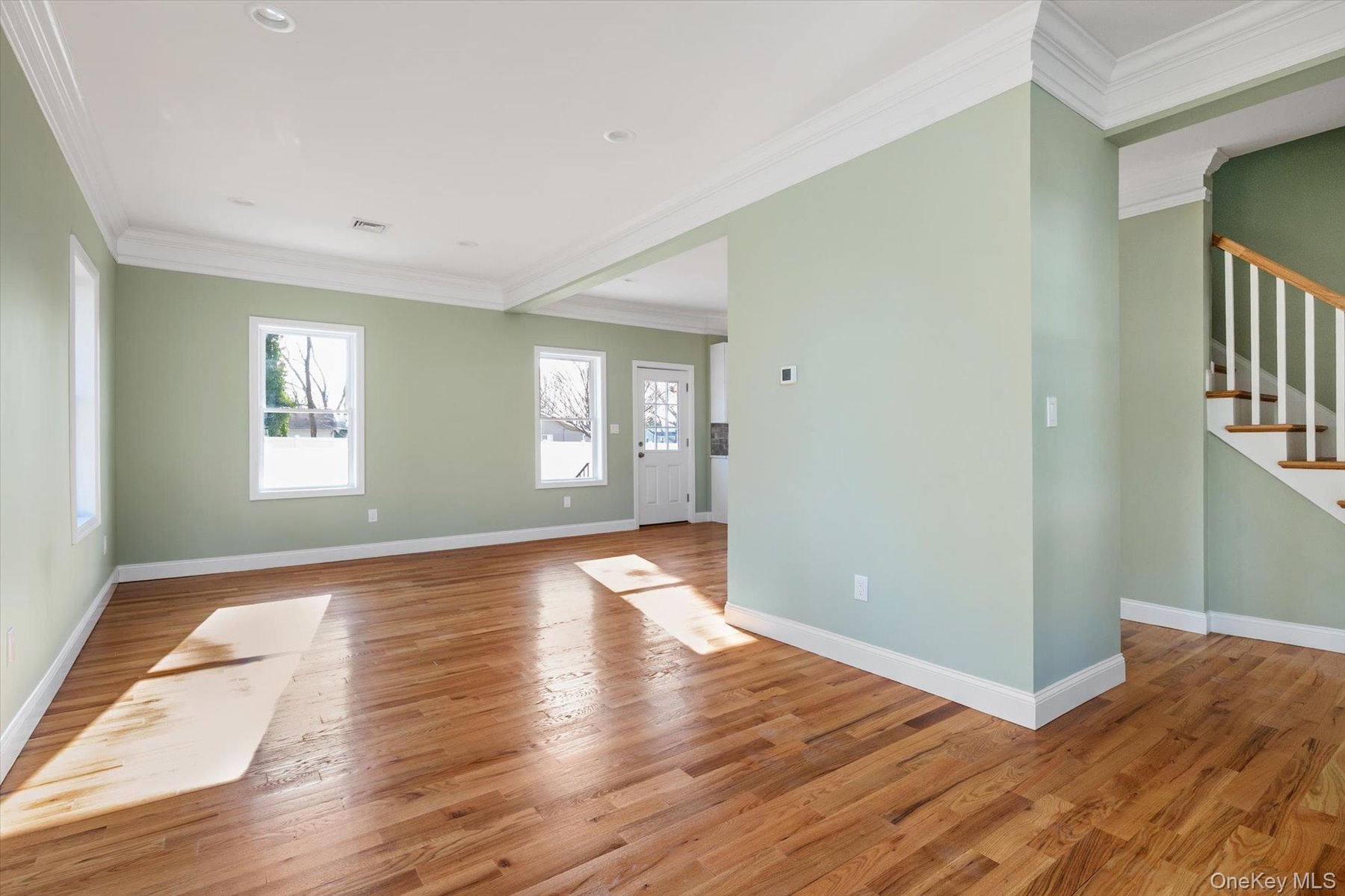 Unfurnished living room with ornamental molding, light wood-style flooring, and stairs