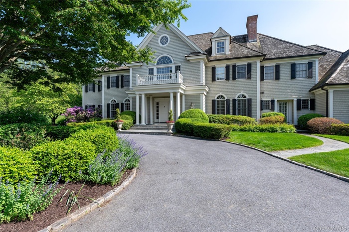 View of front of home with a balcony, a chimney, driveway, and roof with shingles