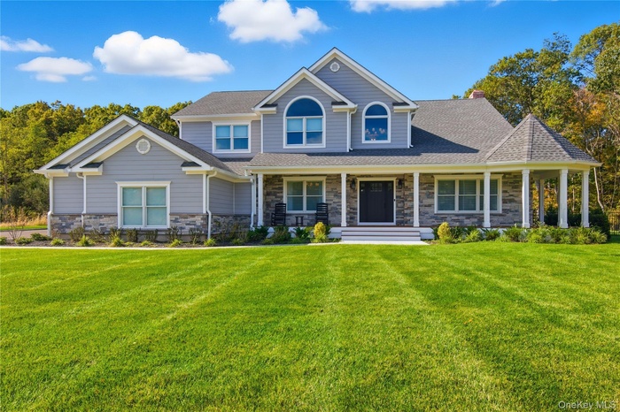 View of front of house with a porch, a front yard, stone siding, and a shingled roof