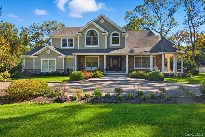 View of front facade featuring stone siding, a porch, a front lawn, and roof with shingles