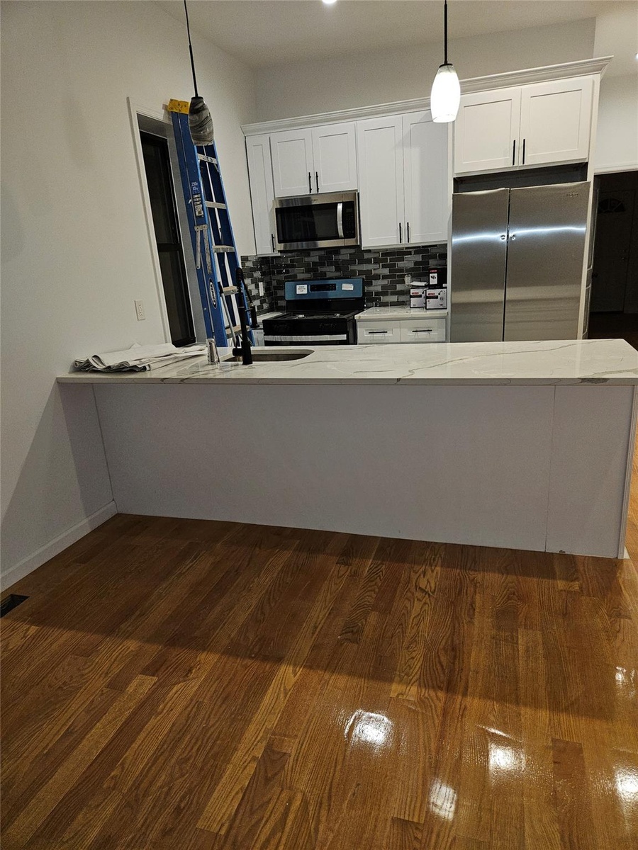 Kitchen with dark wood finished floors, a sink, decorative backsplash, appliances with stainless steel finishes, and white cabinetry