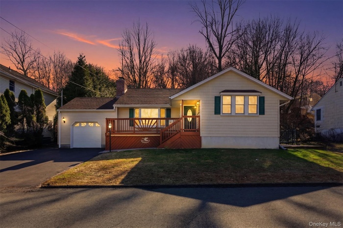 Single story home with a wooden deck, asphalt driveway, a garage, a chimney, and a front yard