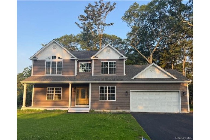 View of front of house with a front lawn, a porch, driveway, a  two car garage, and a shingled roof