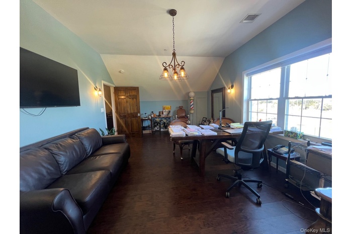 Executive office featuring dark wood-style flooring, lofted ceiling, and a chandelier