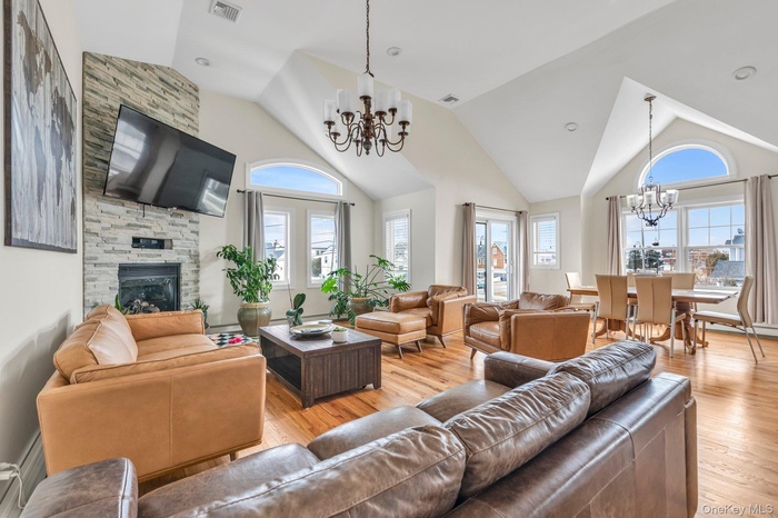 Living room with suspended lighting, a fireplace, light wood-type flooring, and vaulted ceiling
