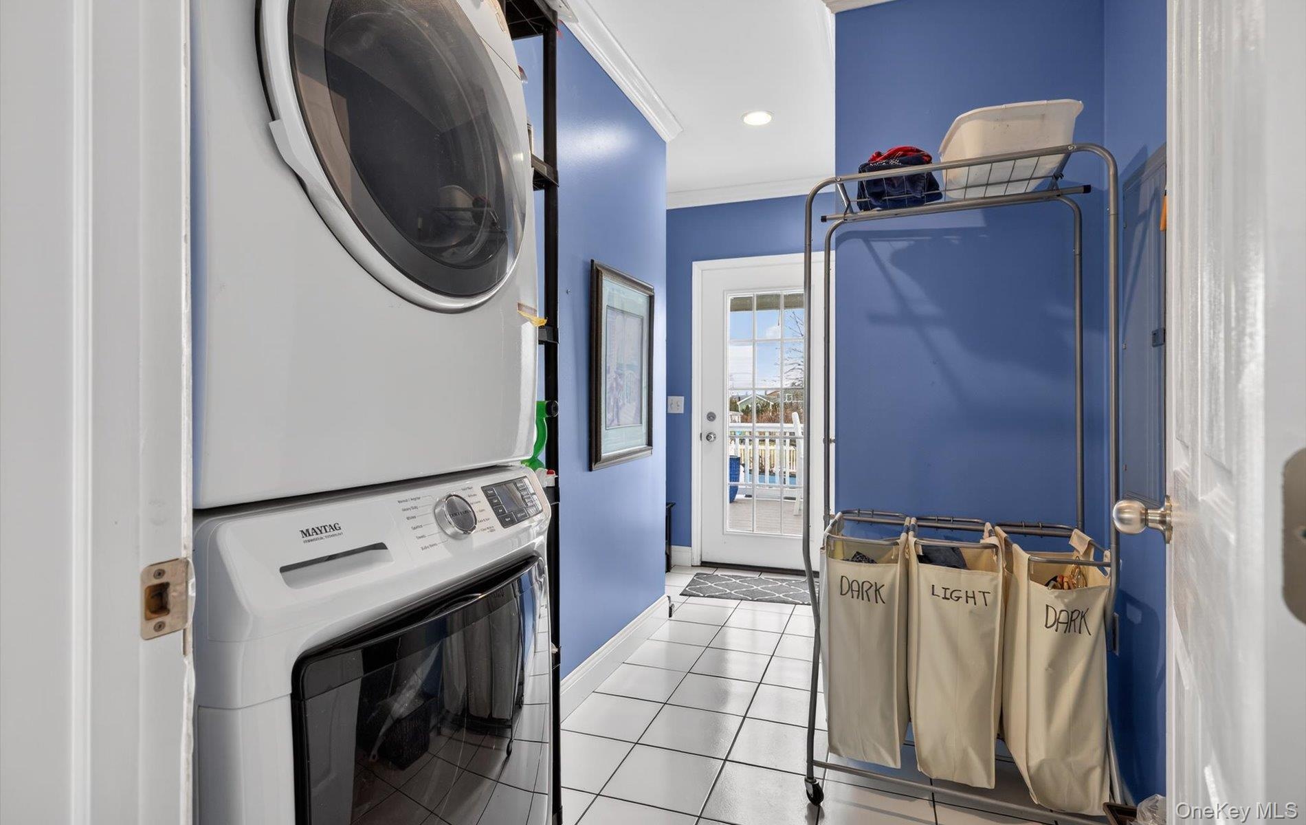 Laundry area with light tile patterned floors, stacked washer and dryer, crown molding, and recessed lighting
