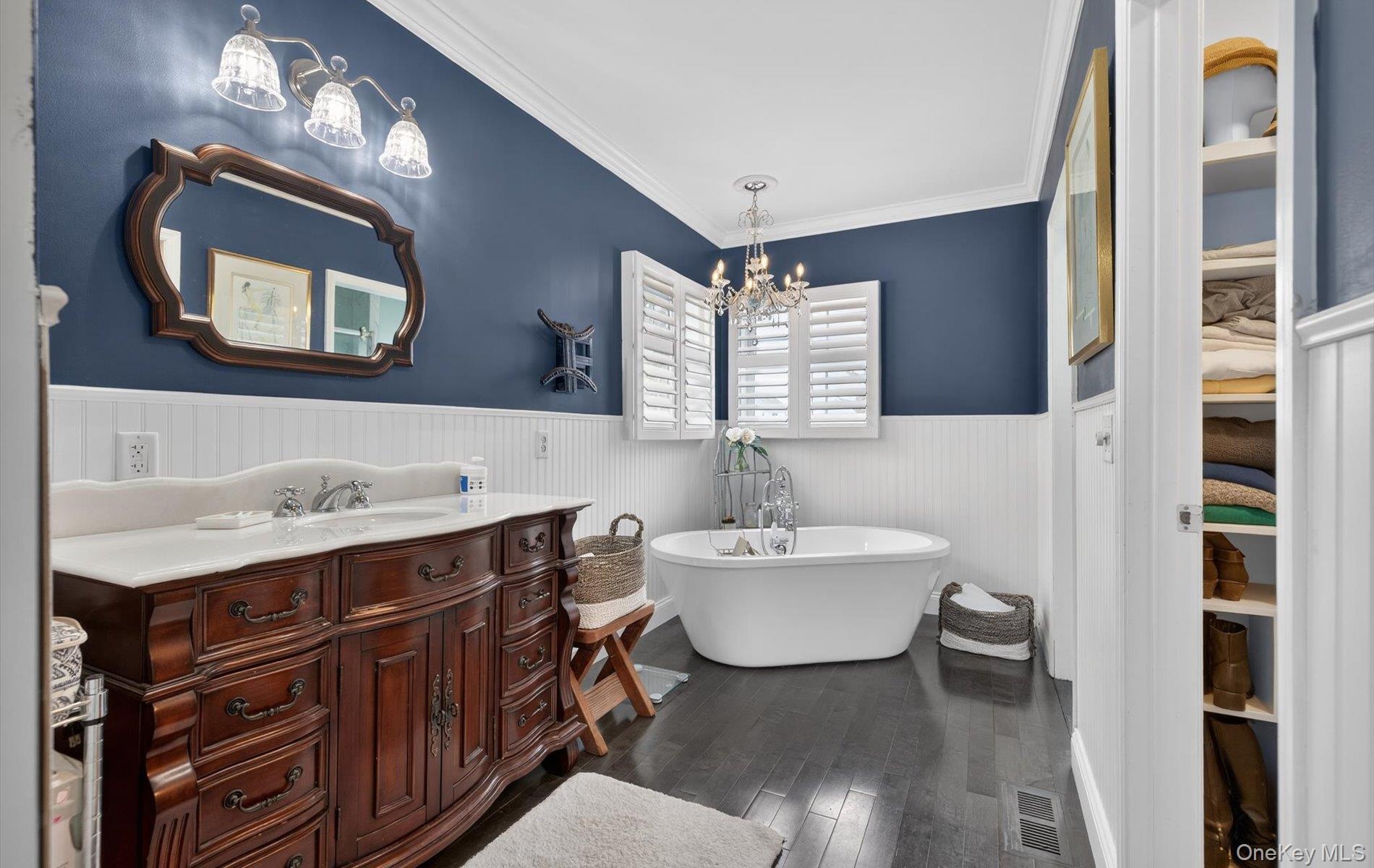 Bathroom featuring vanity, dark wood-style floors, ornamental molding, a freestanding bath, and a wainscoted wall