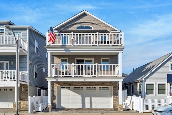 View of front of property featuring stone siding, a balcony, driveway, and an attached garage