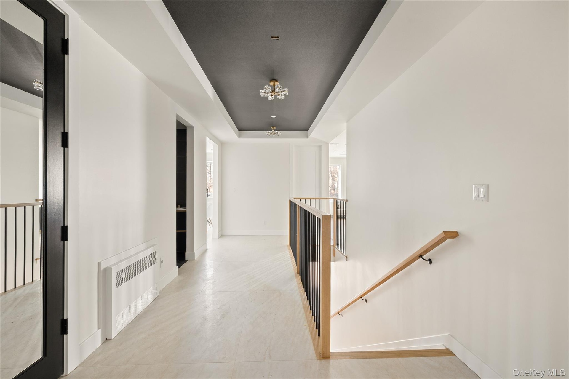 Corridor with an upstairs landing, radiator heating unit, a raised ceiling, and a chandelier