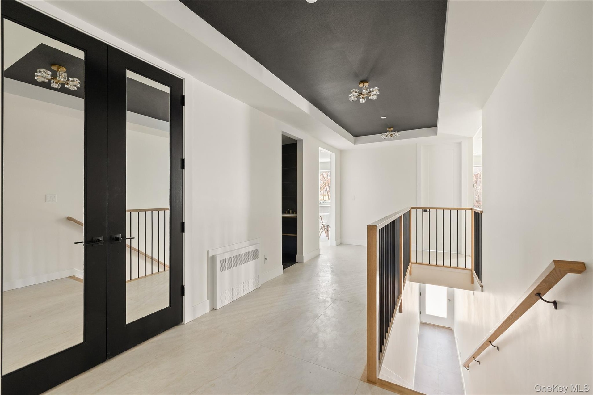 Hallway featuring a tray ceiling, french doors, radiator heating unit, and an upstairs landing