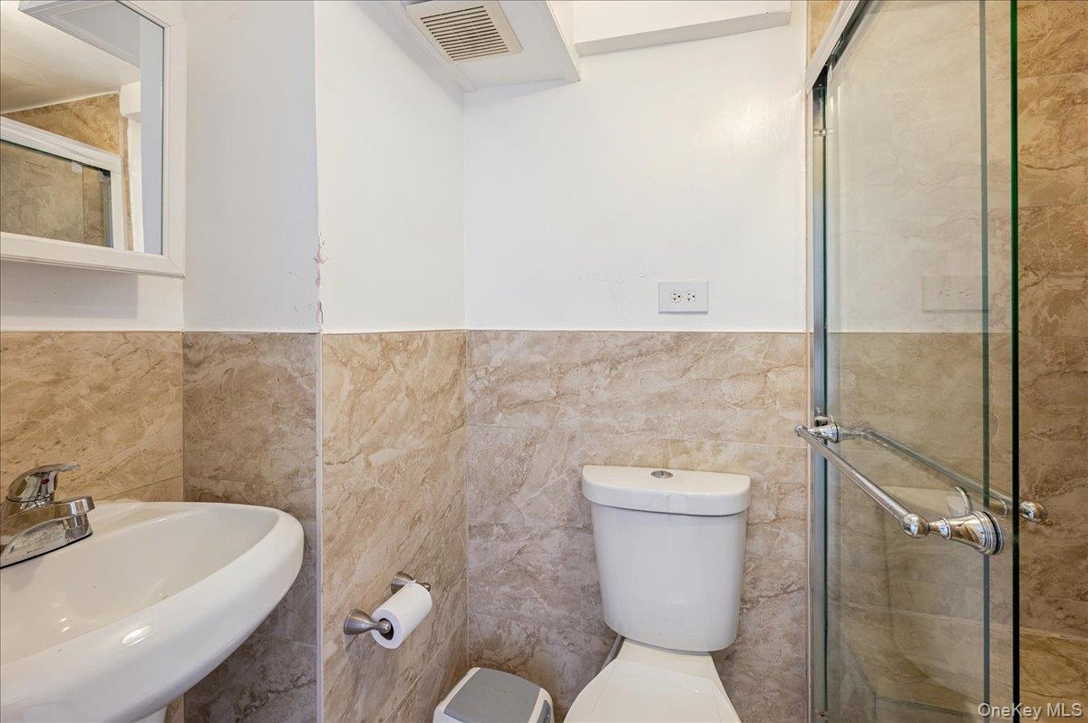 Full second bath featuring a shower stall, a wainscoted wall, and tile walls