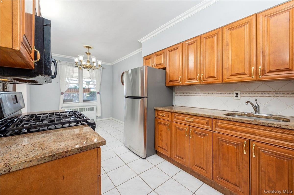 Kitchen featuring wood finish cabinets, light granite countertops, crown molding, stainless steel appliances, and decorative backsplash