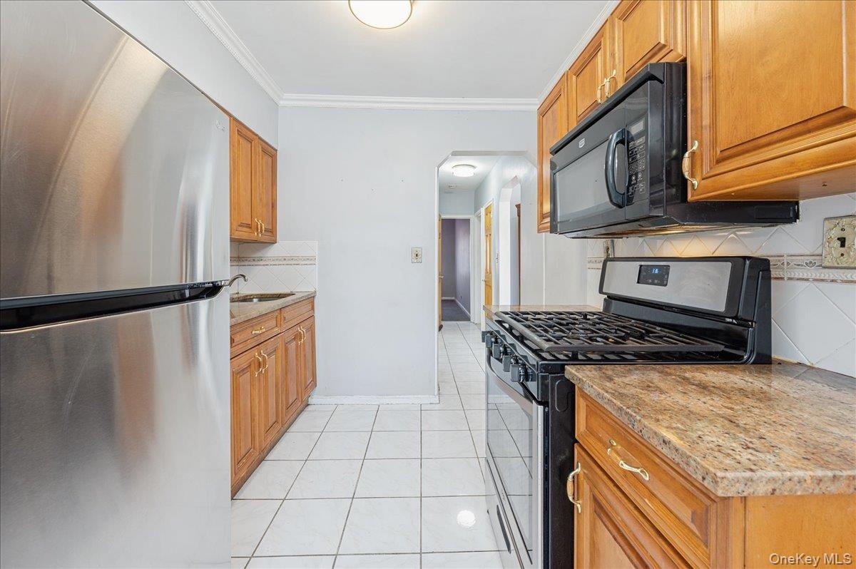Kitchen with stainless steel appliances, light tile patterned floors, crown molding, light stone counters, and decorative backsplash