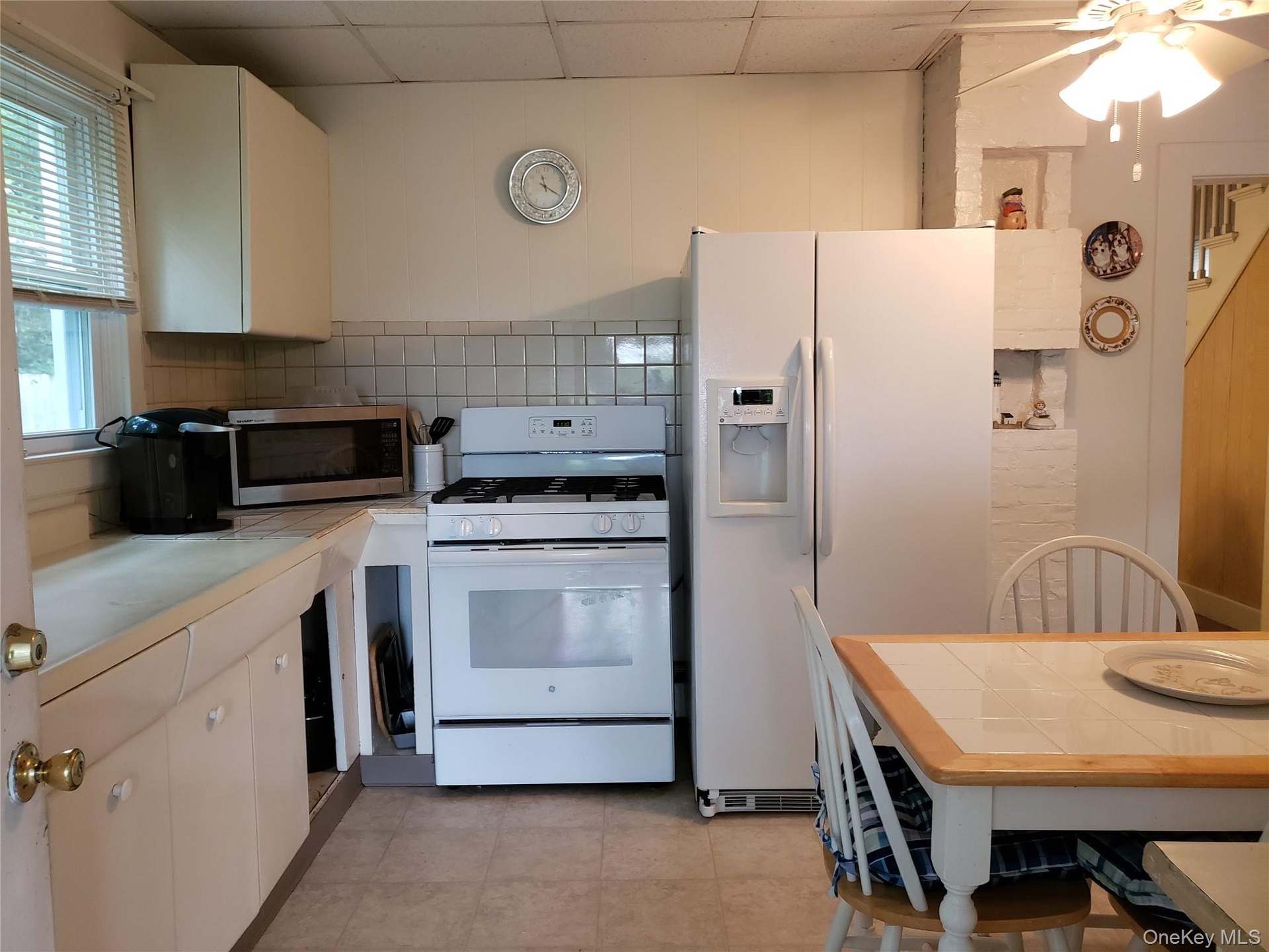 Kitchen with white appliances, a paneled ceiling, a ceiling fan, white cabinetry, and tile counters