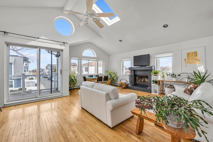 Living room with a ceiling fan, a skylight, light wood-type flooring, a fireplace with raised hearth, and baseboard heating