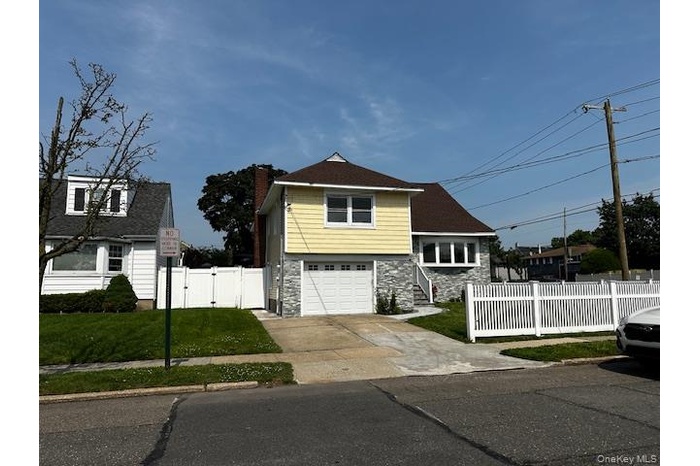 View of front of home with stone siding, a garage, driveway, a gate, and a chimney