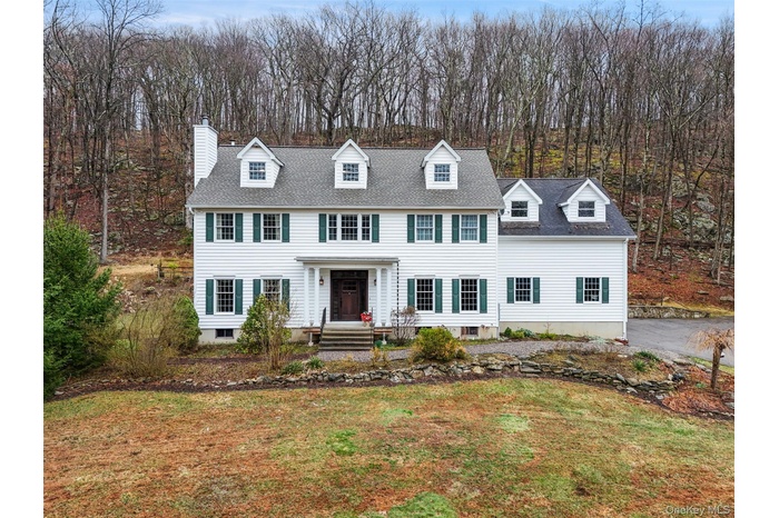 Classic white Colonial with green shutters set on a peaceful, wooded lot, offering timeless curb appeal and serene surroundings.