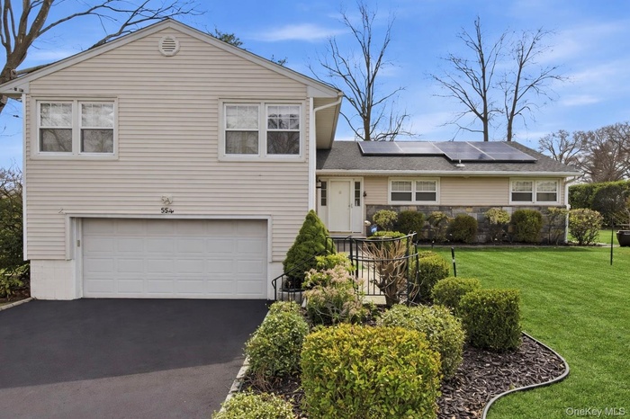 Split level home featuring an attached garage, driveway, a front yard, and roof mounted solar panels