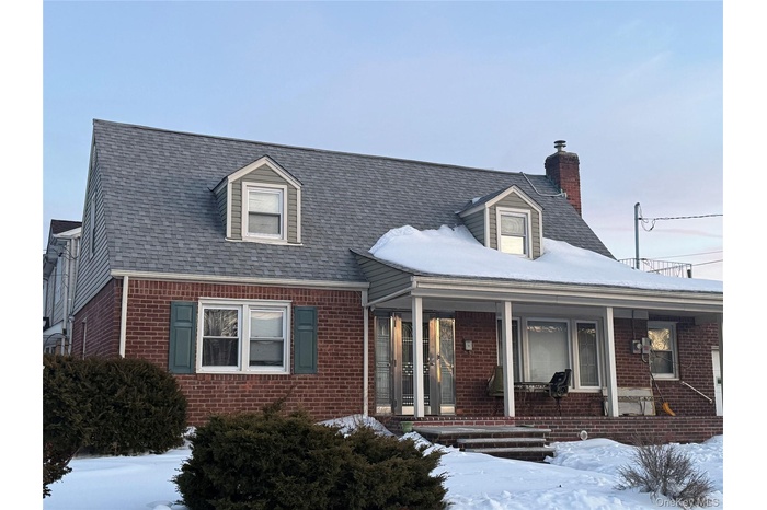 New england style home featuring brick siding, a porch, a chimney, and a shingled roof
