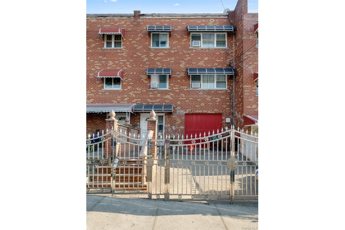 The property features a brick facade with a red garage door and a decorative metal fence