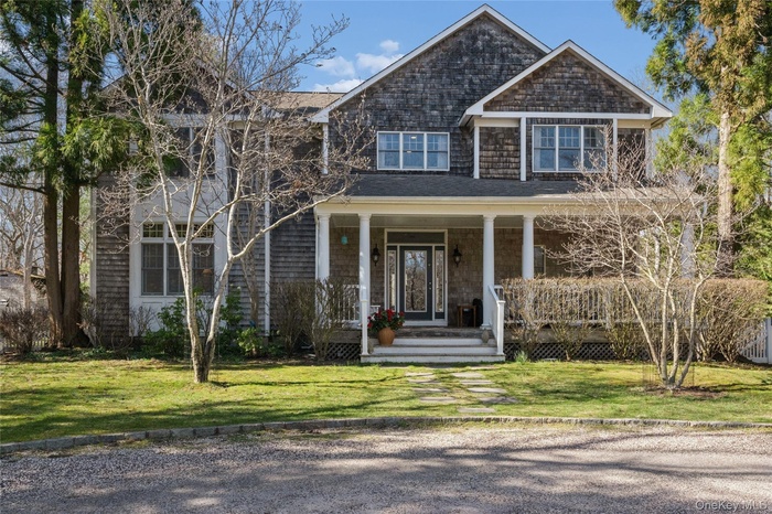 Shingle-style home featuring a front lawn and covered porch, specimen trees waiting to bloom.