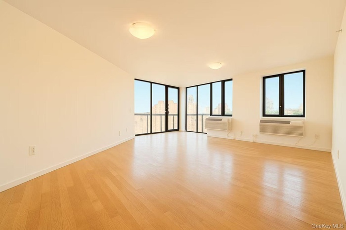 Unfurnished room with light wood-style flooring, a wall of windows, and a wall mounted air conditioner