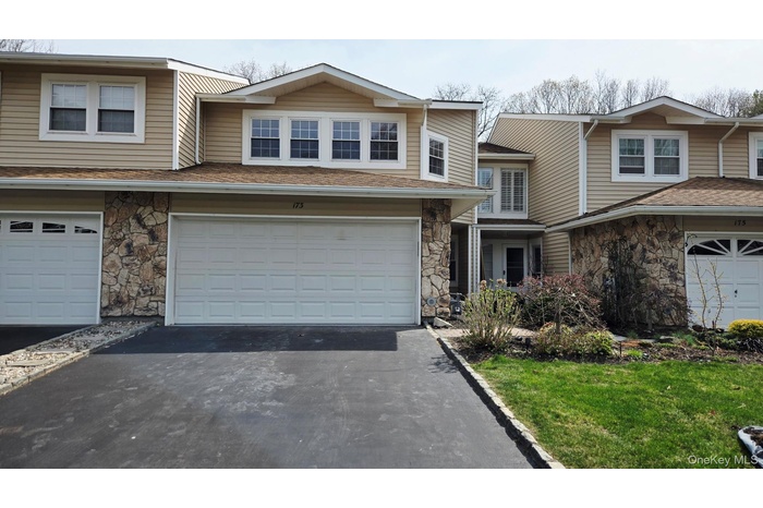 Exterior view of the property showcasing tan siding, stone accents, and a paved driveway leading to a two-car garage