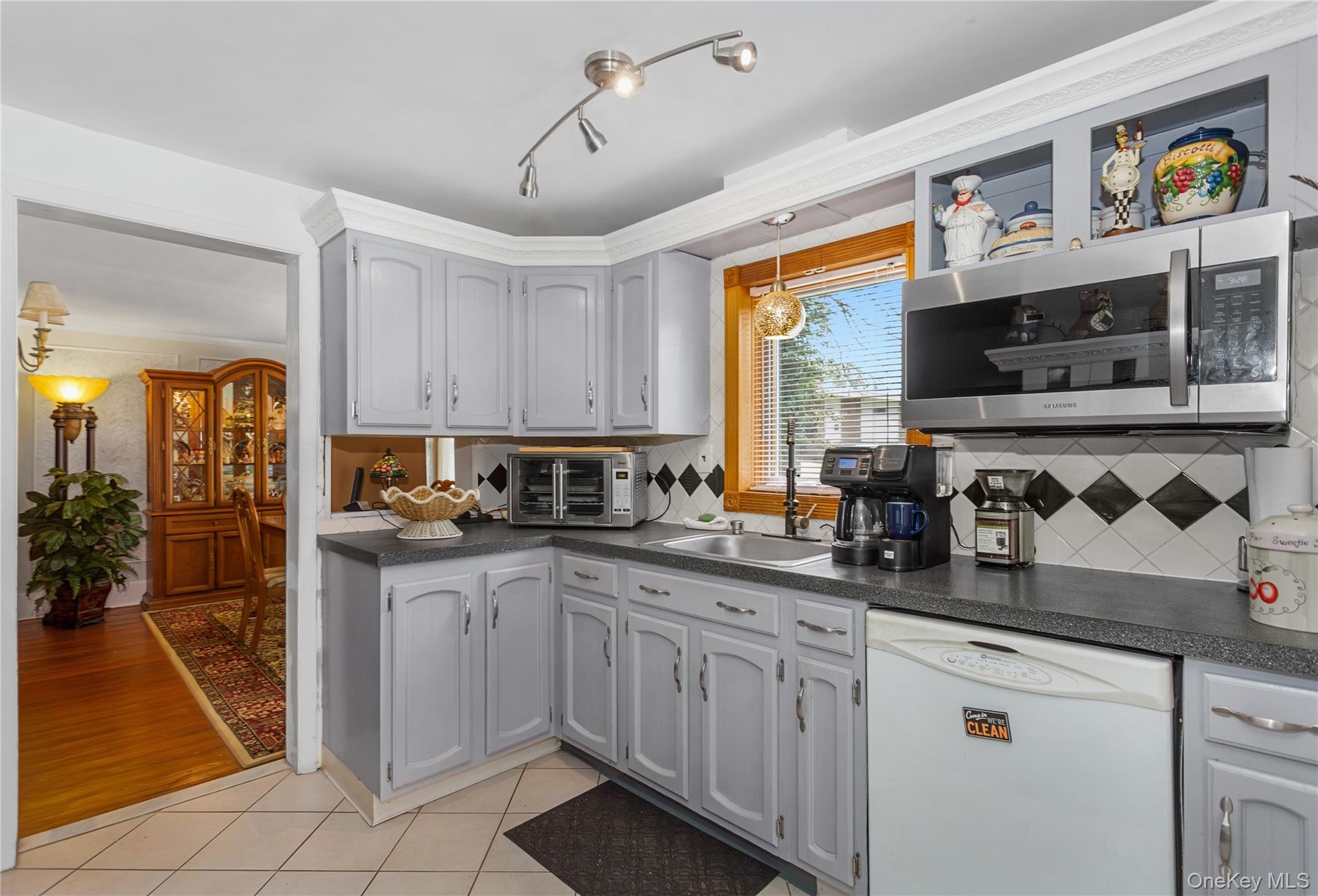 Kitchen with white dishwasher, dark countertops, stainless steel microwave, tasteful backsplash, and crown molding