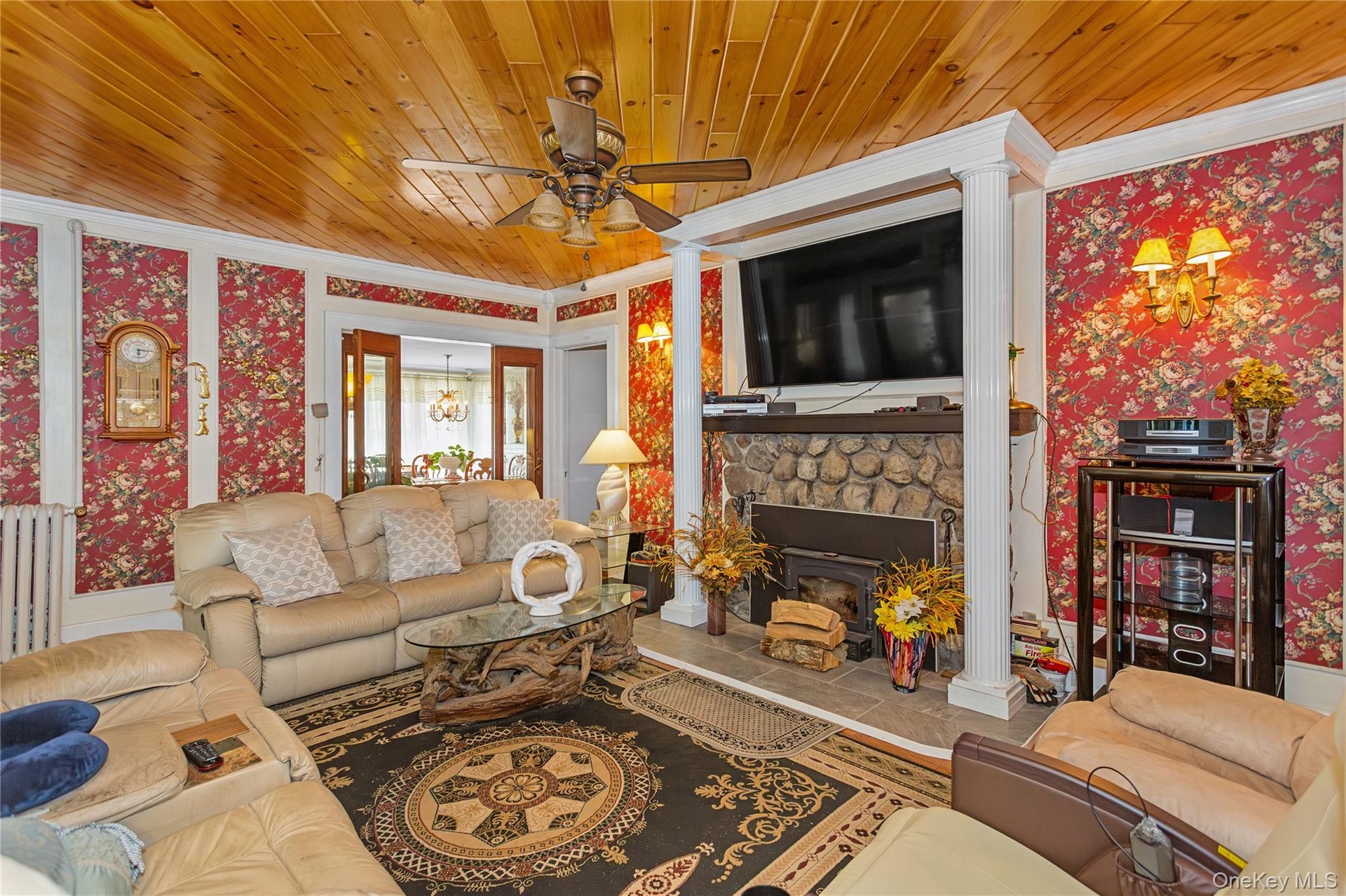 Tiled living room featuring wallpapered walls, wooden ceiling, radiator, a fireplace, and a ceiling fan
