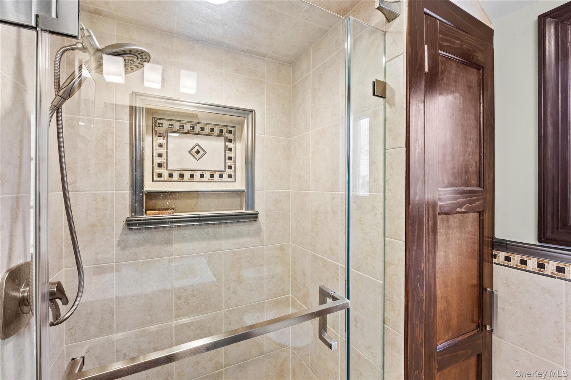 The shower features a handheld showerhead, a tiled niche with decorative accents.