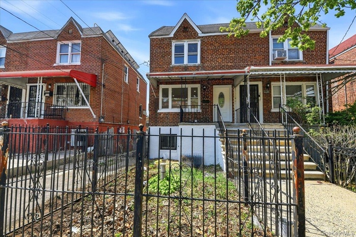 The property features a brick facade, a covered front porch, and a black wrought iron fence