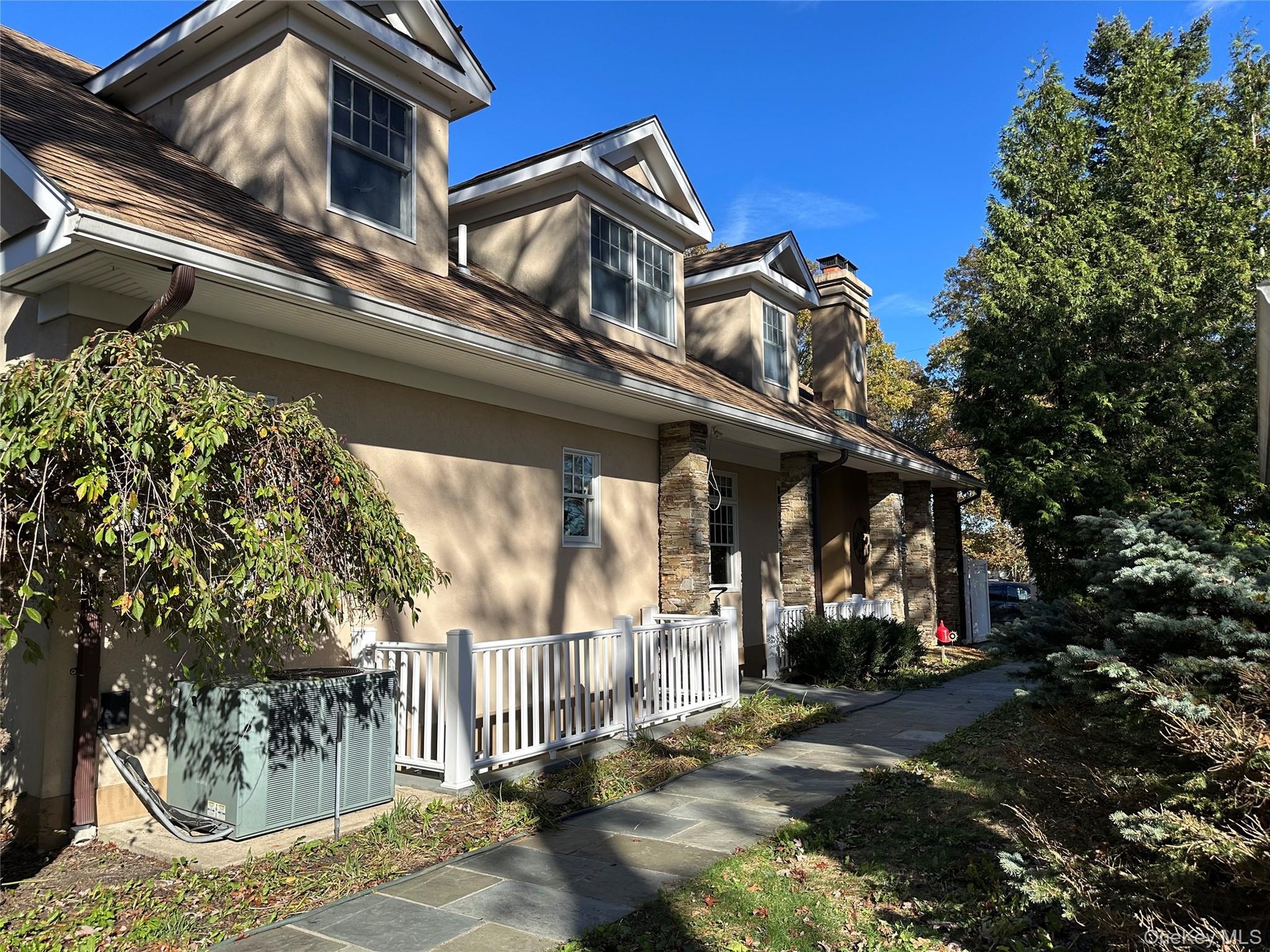 View of side of home featuring stucco facade, covered outside entrance stairs, a chimney, and stone accents
