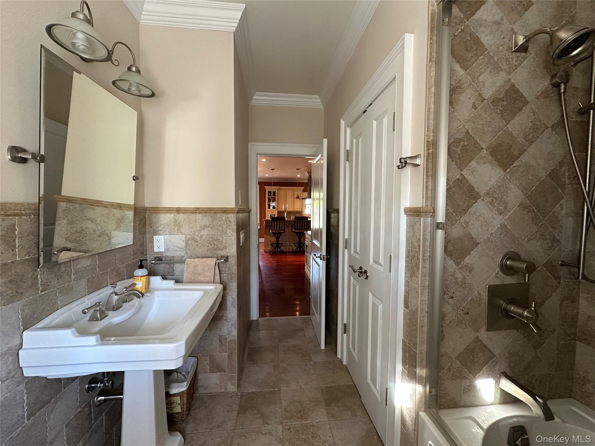 Full bath with tile walls, crown molding, a wainscoted wall, and bathing tub / shower combination